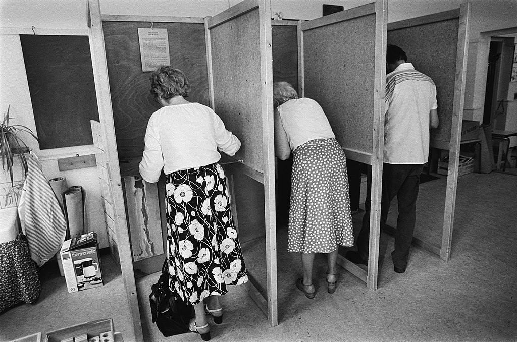 Foto van drie stemmers in een stemhokje tijden de gemeenteraadsverkiezingen van 1982