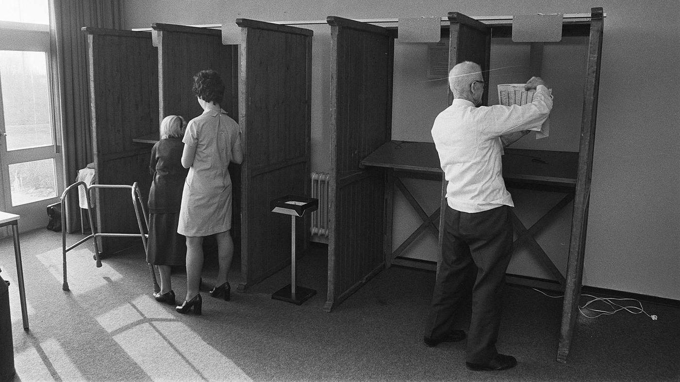 Stemmen in de jaren vijftig. Kiezers in stemhokjes vullen hun stemformulier in.