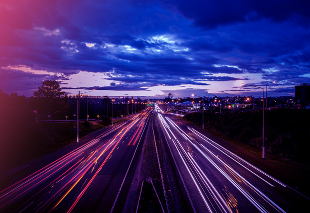 Een lange weg met lichtsporen van auto's onder een donkere, bewolkte avondhemel.