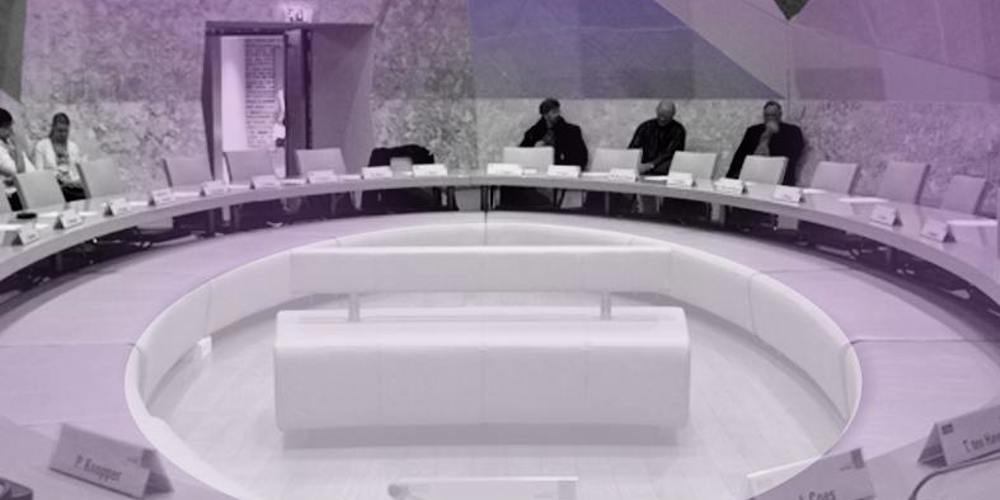 Een vergaderruimte met een grote, ovale tafel waar mensen aan zitten.