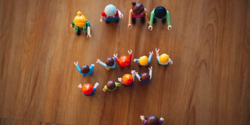 Playmobil op een houten vloer, van bovenaf gefotografeerd. De poppetjes stellen twee groepen voor die tegenover elkaar staan. 