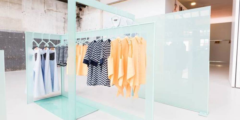 Moderne kledingdisplay in een minimalistische winkel met pastelgroene rekken en stijlvolle kledingstukken in blauw, wit en perzik.