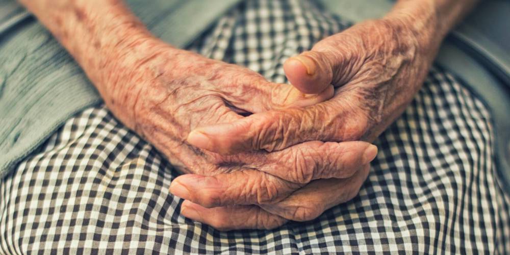 Oude gevouwen handen op een schoot met een geruite schort.