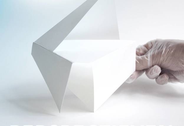 Foto: Een hand met een transparante handschoen houdt een abstract, wit papieren object vast. Het object heeft scherpe hoeken en een opwaarts wijzende vorm. Op de afbeelding staat het woord 'PERSPECTIEVEN' in grote letters.