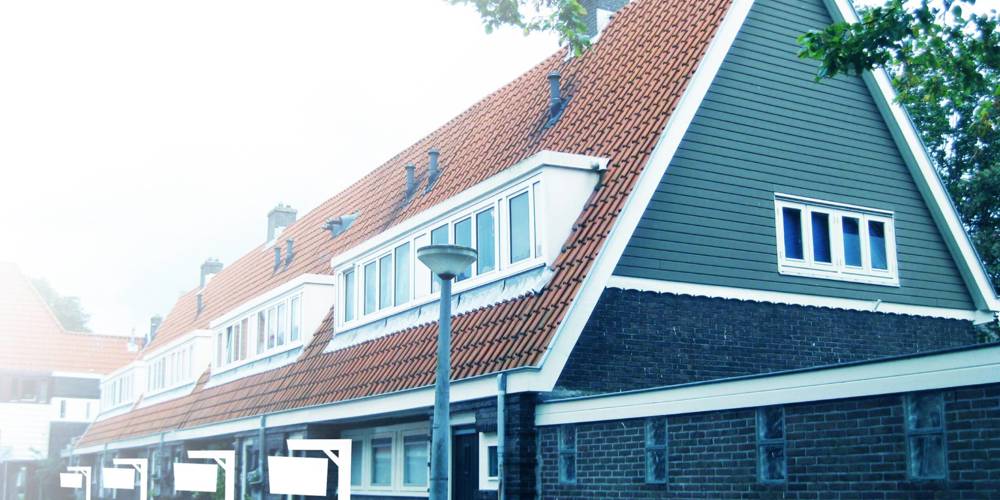 Een foto van een rij rijtjeshuizen met een opvallend oranje dak en een groene gevelbekleding. De huizen hebben witte kozijnen en een donkere bakstenen onderkant.